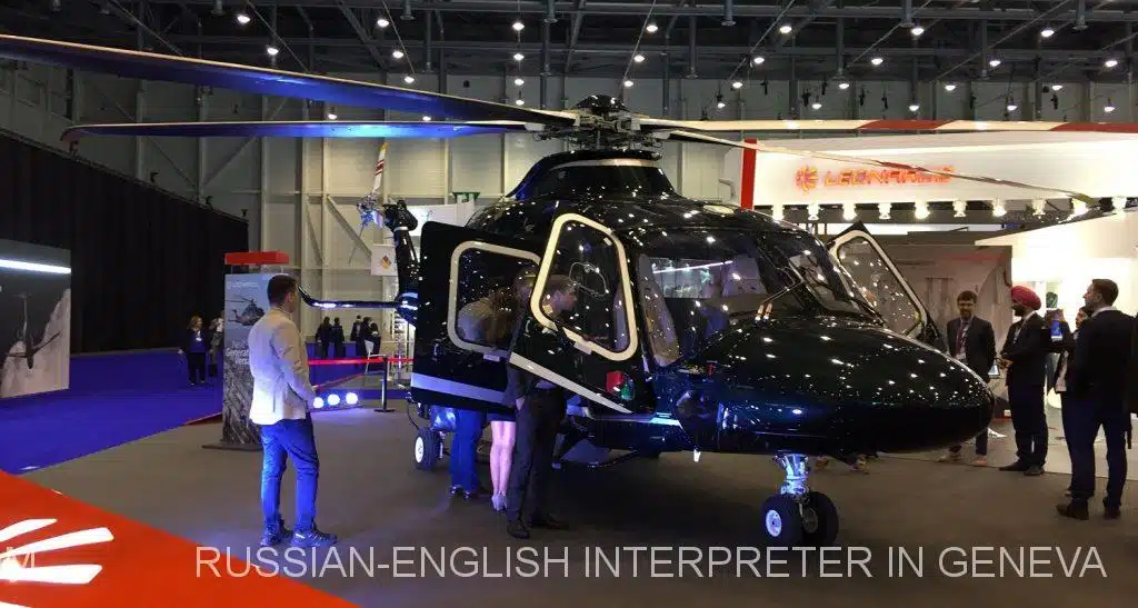 A professional Russian-English interpreter at the European Business Aviation Exhibition (EBACE) in Geneva, Palexpo, Switzerland, actively facilitating communication between international aviation professionals. The setting showcases the modern and spacious halls of Palexpo, filled with cutting-edge private jets, aviation displays, and business booths. The interpreter is seen assisting during a high-level business discussion, ensuring seamless translation and interpretation for attendees. The vibrant atmosphere highlights global collaboration in the aviation industry, with professionals exchanging ideas, forming partnerships, and exploring innovative solutions. The interpreter, with a notepad and headset, embodies professionalism and expertise in providing translation services tailored to the event.